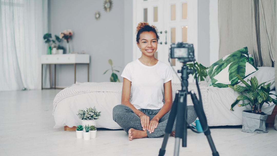 Good-looking African American girl creative blogger is recording video about plants sitting on floor of her modern apartment and talking looking at camera on tripod.