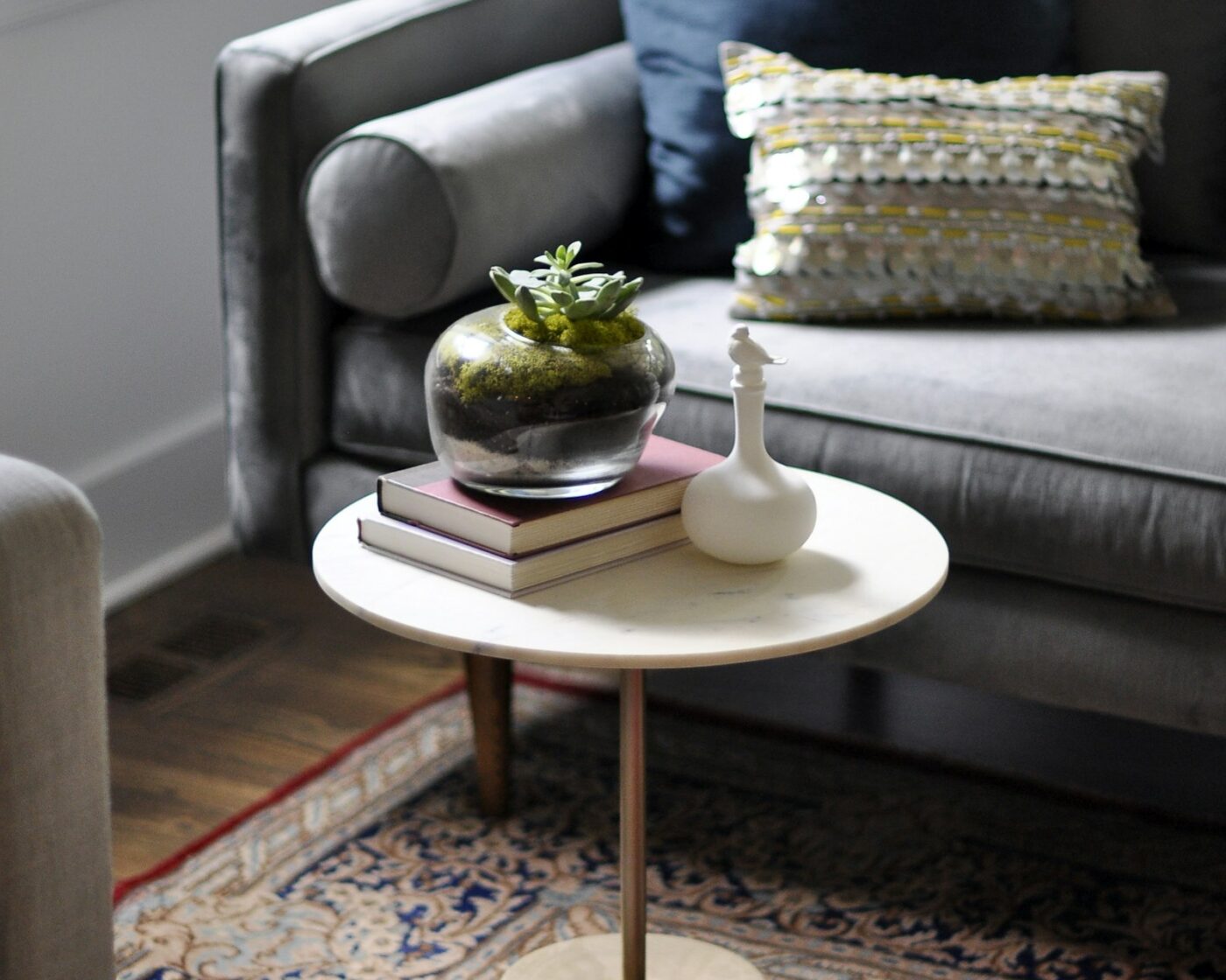 Ronde salontafel met boeken en plant naast een grijze bank