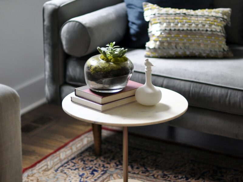 Ronde salontafel met boeken en plant naast een grijze bank
