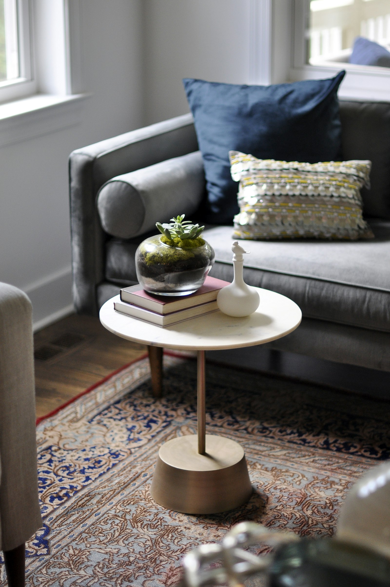 Ronde salontafel met boeken en plant naast een grijze bank