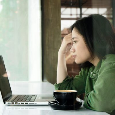 Vrouw die twijfelend naar haar laptop kijkt tijdens het werk