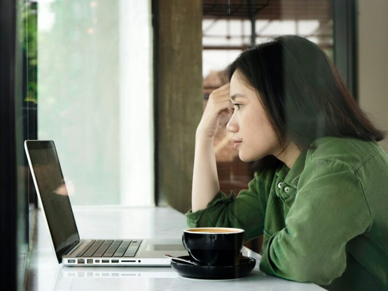 Vrouw die twijfelend naar haar laptop kijkt tijdens het werk