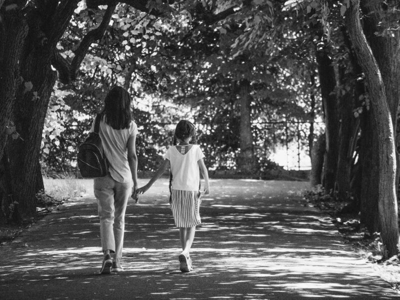 Volwassen dochter loopt arm in arm met haar oudere moeder over een pad in het park