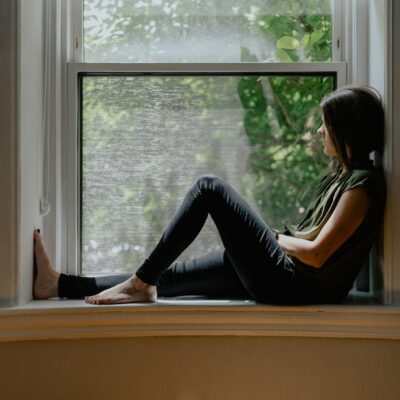 Vrouw zit rechtop op een stoel bij het raam met de ogen dicht