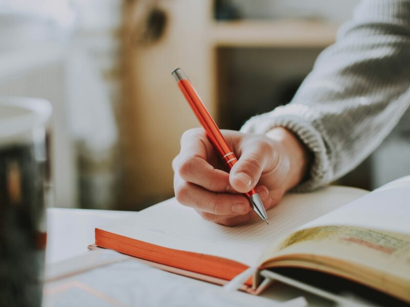 Student maakt aantekeningen in een schrift aan een houten tafel