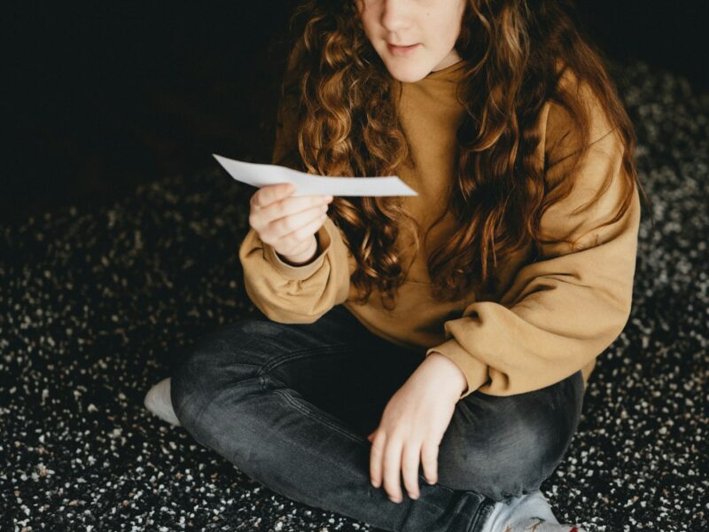 Vrouw zit vermoeid aan een keukentafel met een brief en een kop thee