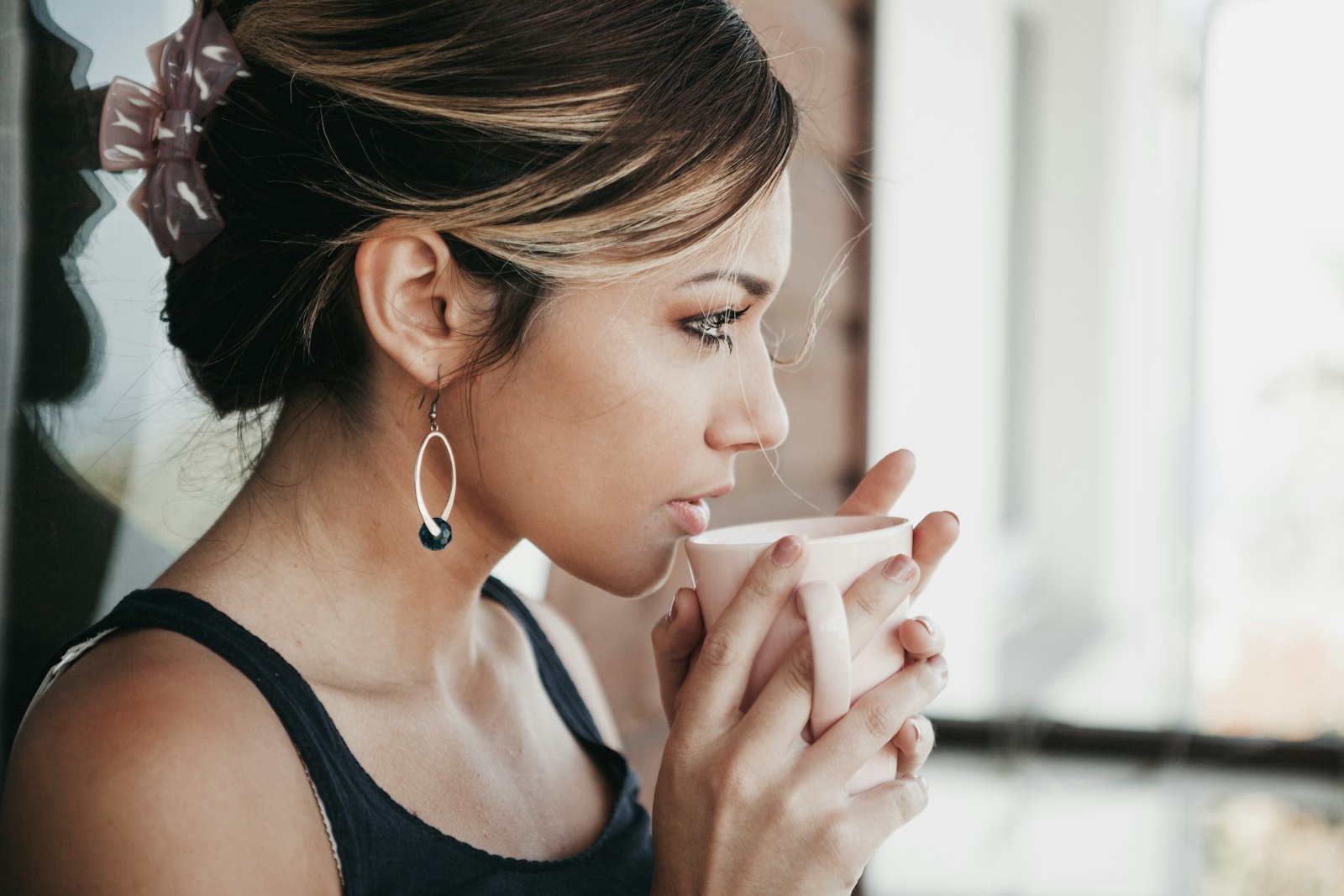 Vrouw zit rustig met een kop thee bij het raam en kijkt naar buiten