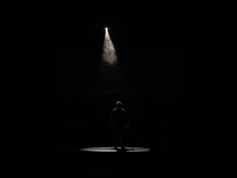 Zanger met microfoon op een groot concertpodium in felle spotlights