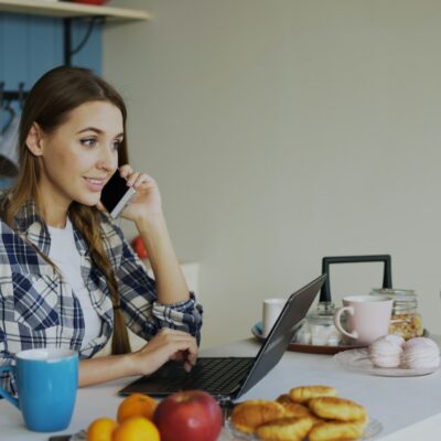 Vrouw werkt op een laptop aan de keukentafel thuis met een kop koffie