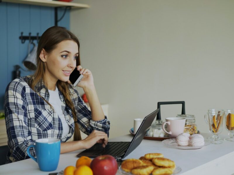 Vrouw werkt op een laptop aan de keukentafel thuis met een kop koffie